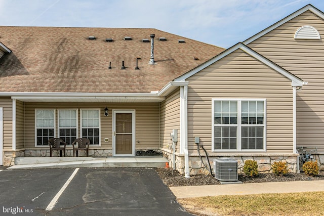 view of front of home featuring uncovered parking, central AC unit, stone siding, and a shingled roof