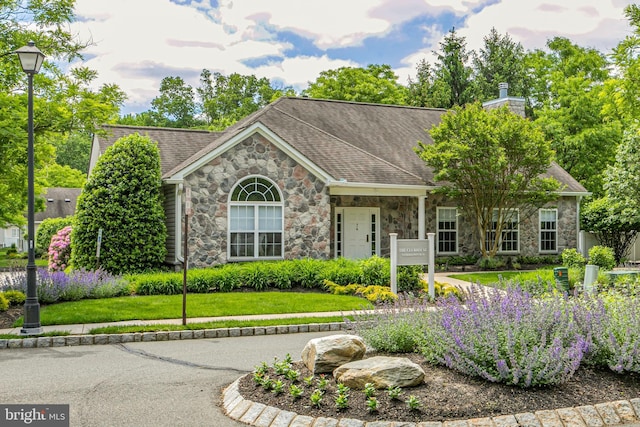 view of front of home featuring a front yard, stone siding, and roof with shingles