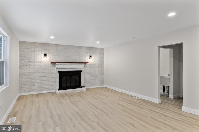 unfurnished living room with visible vents, baseboards, brick wall, wood finished floors, and a brick fireplace