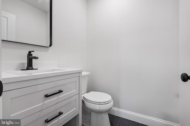 half bath with toilet, tile patterned floors, baseboards, and vanity