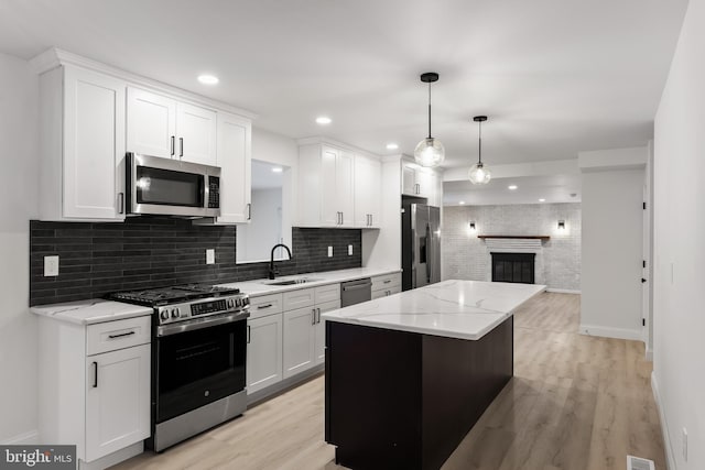 kitchen with a brick fireplace, light wood-style flooring, stainless steel appliances, and a sink