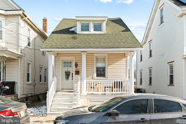 view of front of property featuring a porch, cooling unit, and roof with shingles