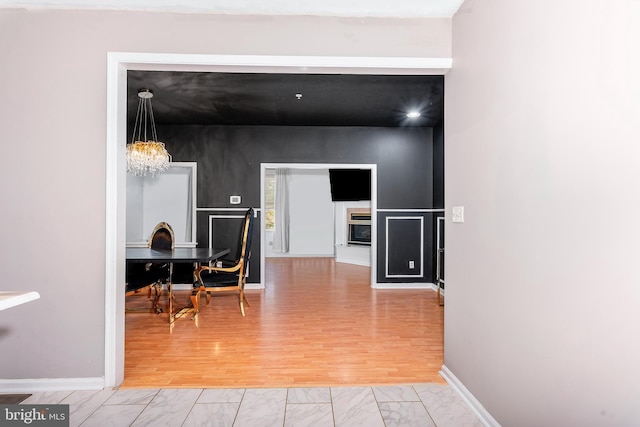 corridor featuring baseboards, wood finished floors, and a chandelier
