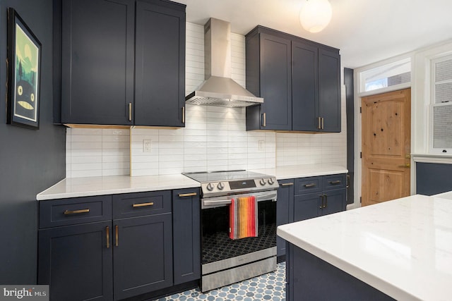 kitchen featuring light stone counters, stainless steel electric stove, backsplash, and wall chimney range hood