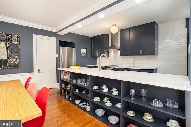 kitchen with light wood-type flooring, light countertops, wall chimney exhaust hood, and open shelves