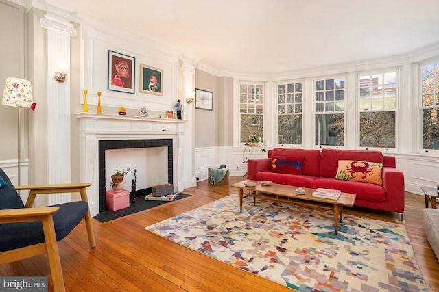 living area with a decorative wall, crown molding, a fireplace with flush hearth, and wood-type flooring