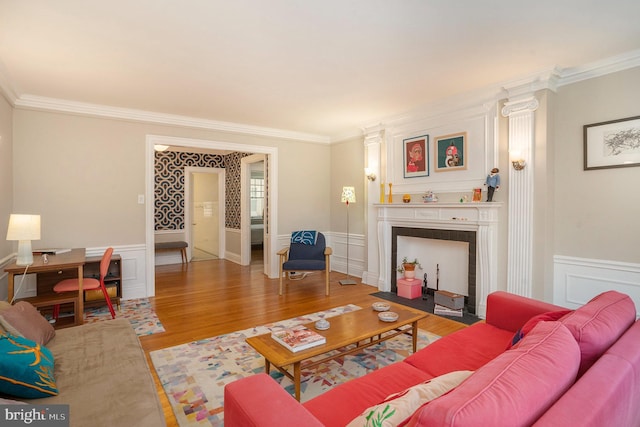 living room featuring wainscoting, wood finished floors, a fireplace, and ornamental molding