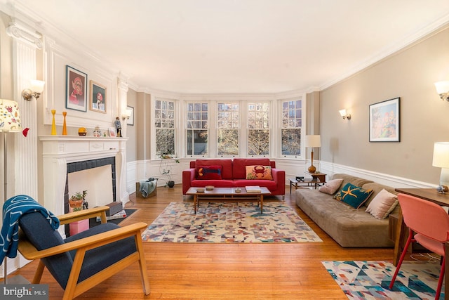 living room featuring a fireplace with flush hearth, wood finished floors, wainscoting, and ornamental molding