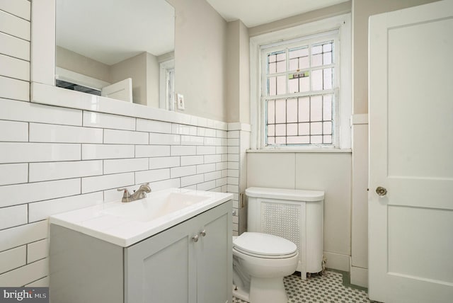 half bath featuring toilet, tile walls, wainscoting, and vanity