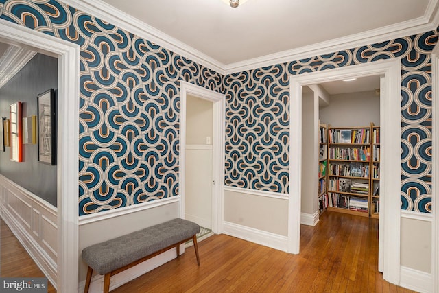 interior space with wood finished floors, crown molding, and wallpapered walls