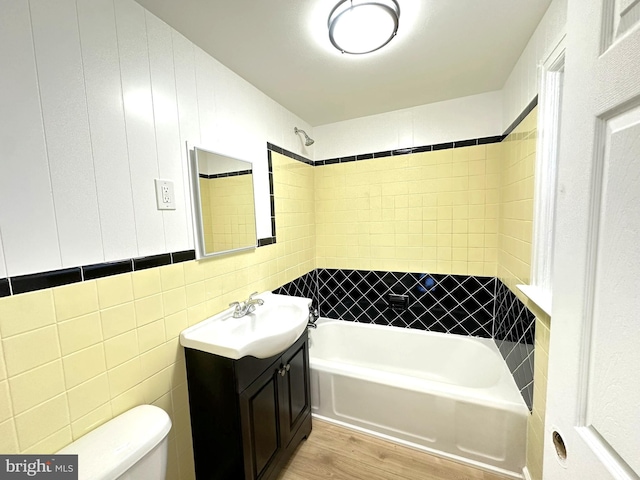 full bathroom featuring toilet, shower / tub combination, wood finished floors, tile walls, and vanity