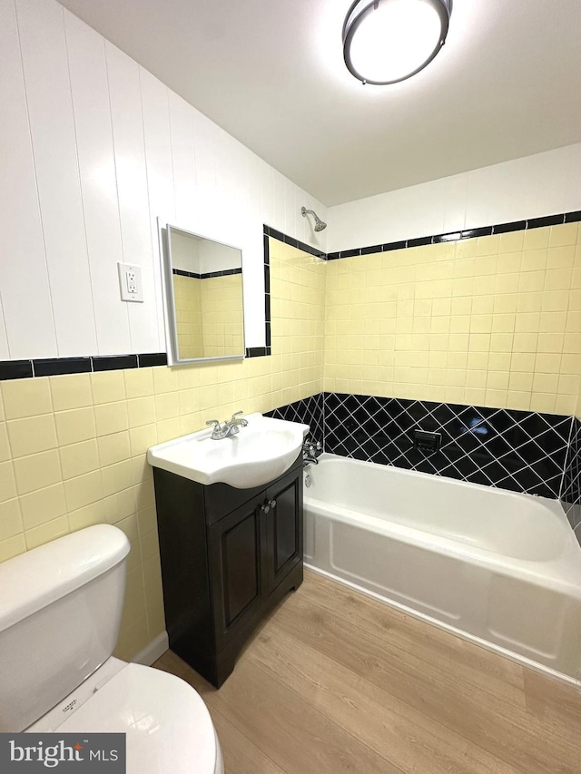 bathroom featuring vanity, wood finished floors, shower / tub combination, toilet, and tile walls