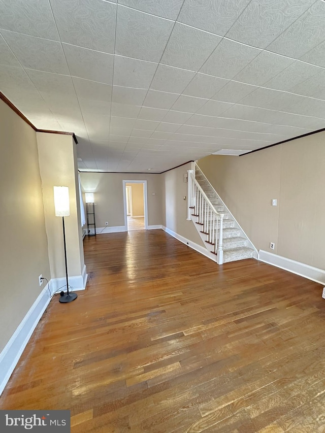 unfurnished living room featuring baseboards, wood finished floors, and stairs