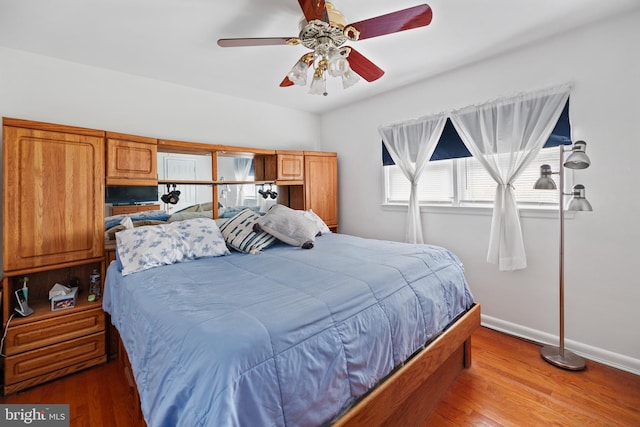 bedroom featuring baseboards, wood finished floors, and a ceiling fan