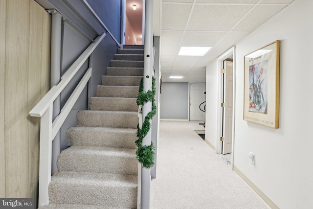 staircase featuring a drop ceiling, carpet floors, and baseboards