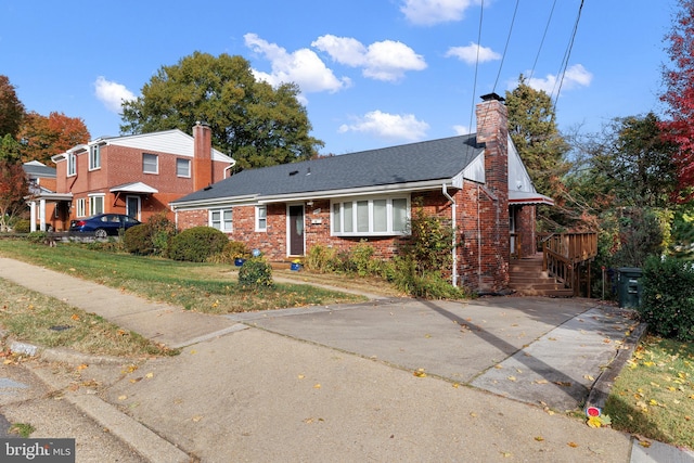 view of front of house featuring a shingled roof, a front yard, brick siding, and a chimney