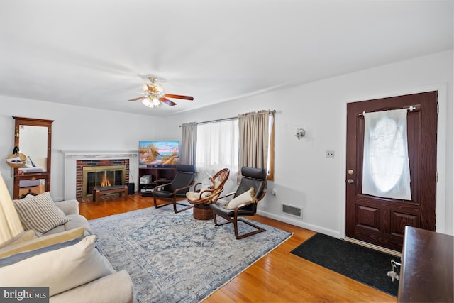 living room with visible vents, baseboards, light wood-type flooring, a fireplace, and a ceiling fan