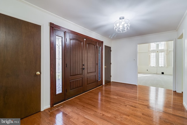 foyer entrance with wood finished floors, baseboards, visible vents, ornamental molding, and a notable chandelier