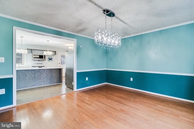 unfurnished dining area with ornamental molding, an ornate ceiling, baseboards, and wood finished floors