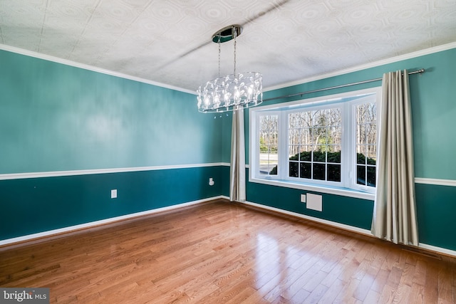 empty room featuring baseboards, ornamental molding, an inviting chandelier, wood finished floors, and an ornate ceiling