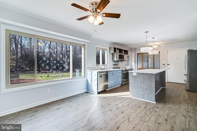 kitchen with a kitchen island, light countertops, appliances with stainless steel finishes, wood finished floors, and a sink