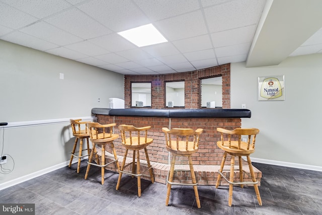 bar featuring a drop ceiling, baseboards, a dry bar, and brick wall