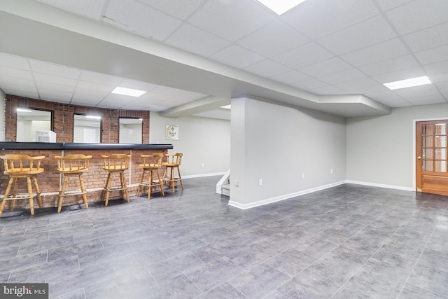 bar featuring a dry bar, a paneled ceiling, baseboards, and brick wall