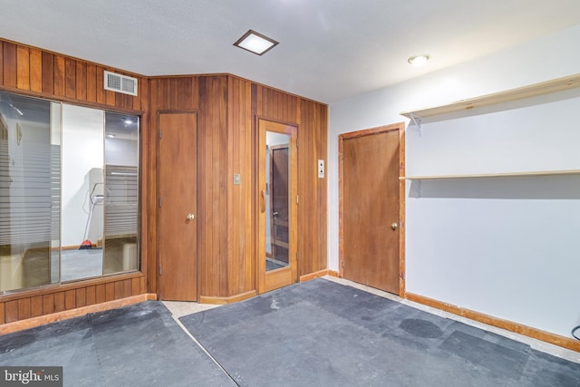 unfurnished bedroom with visible vents, concrete floors, wood walls, and a closet