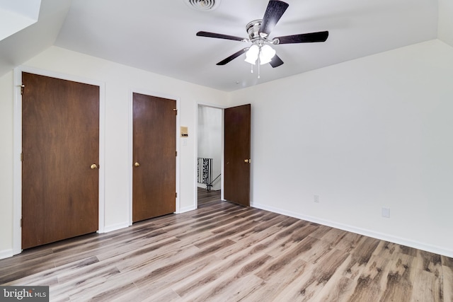 unfurnished bedroom featuring baseboards, lofted ceiling, multiple closets, and wood finished floors