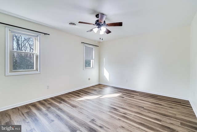 empty room with visible vents, ceiling fan, baseboards, and wood finished floors