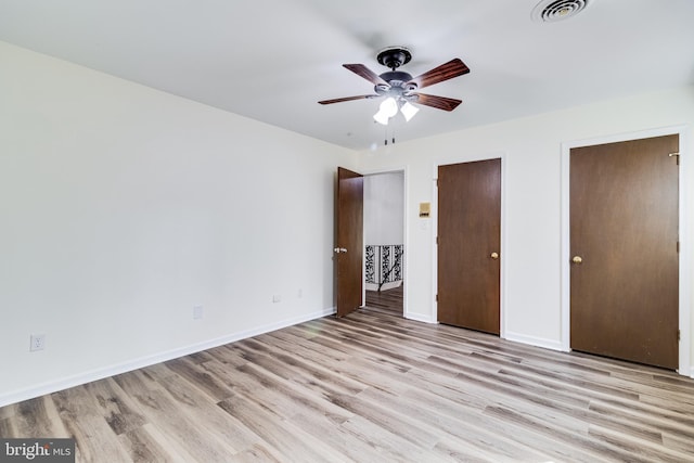 unfurnished bedroom with baseboards, visible vents, light wood-style flooring, ceiling fan, and multiple closets