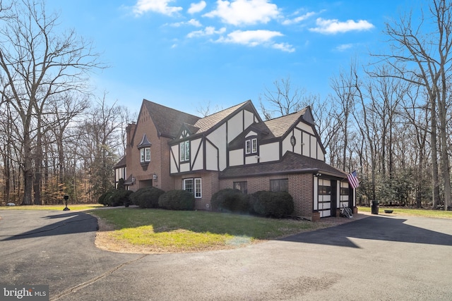 view of property exterior with a shingled roof, stucco siding, aphalt driveway, a lawn, and brick siding