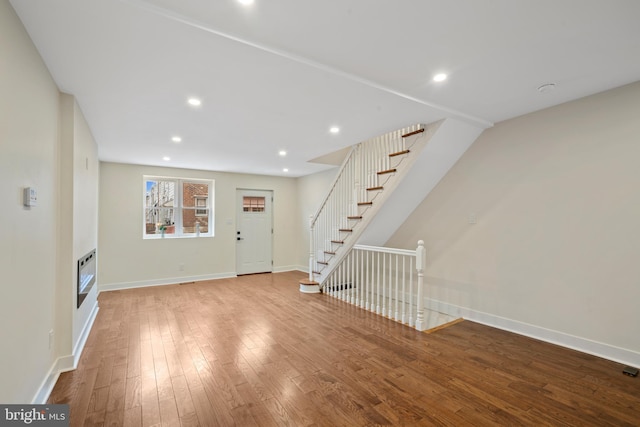 unfurnished living room featuring baseboards, stairway, recessed lighting, a glass covered fireplace, and wood-type flooring