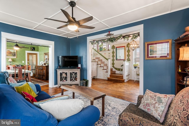 living area featuring ceiling fan with notable chandelier, stairs, and wood finished floors