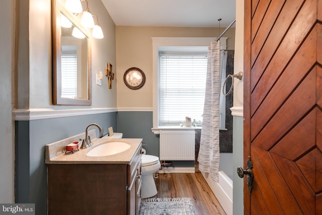 full bathroom featuring toilet, radiator heating unit, wood finished floors, and a wealth of natural light