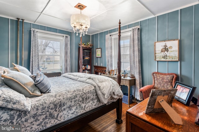 bedroom featuring a notable chandelier, wood finished floors, ornamental molding, and a decorative wall