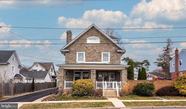 view of front of home featuring stone siding, a porch, a chimney, and fence