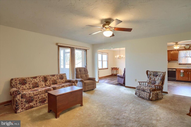 living area with light carpet, a healthy amount of sunlight, and ceiling fan with notable chandelier