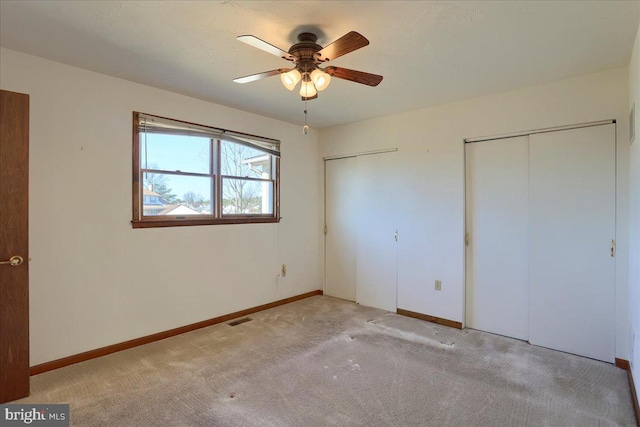 unfurnished bedroom featuring visible vents, multiple closets, a ceiling fan, baseboards, and light colored carpet