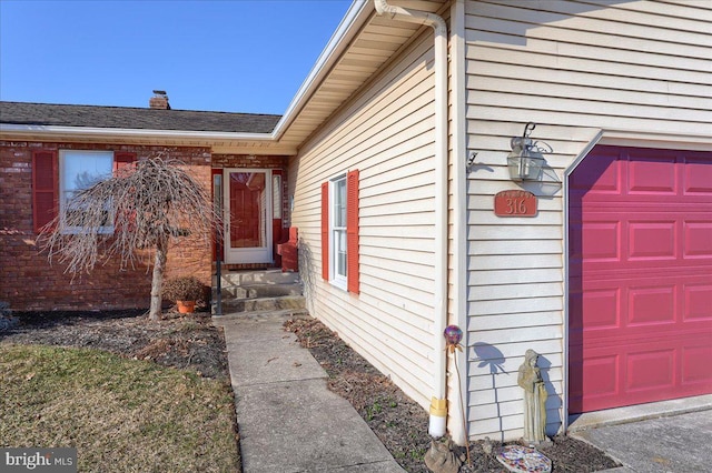 entrance to property with an attached garage, a chimney, and a shingled roof