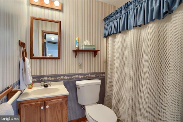 bathroom featuring curtained shower, toilet, vanity, and wallpapered walls