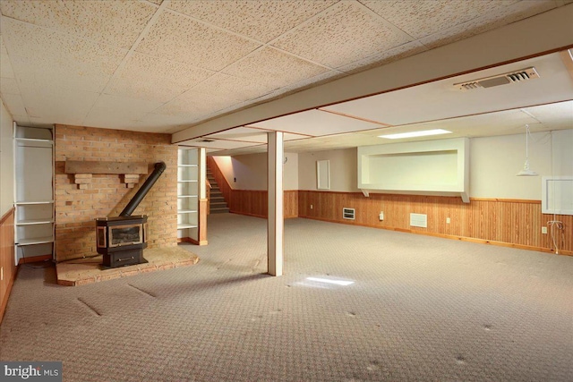 finished below grade area with a wood stove, visible vents, wood walls, and wainscoting