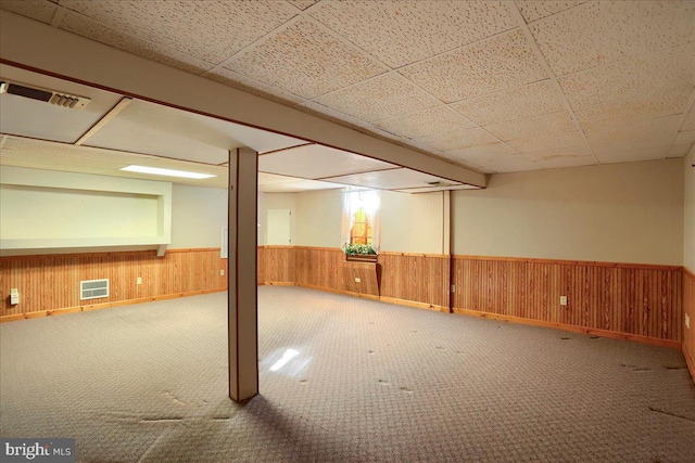 finished below grade area featuring visible vents, a paneled ceiling, wood walls, and wainscoting