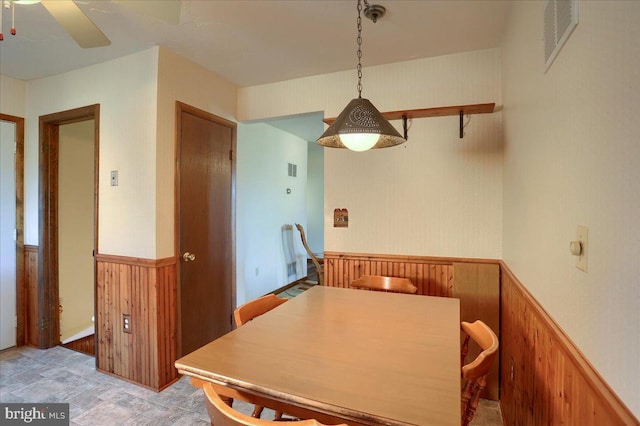 dining space featuring a ceiling fan, visible vents, a wainscoted wall, and wood walls