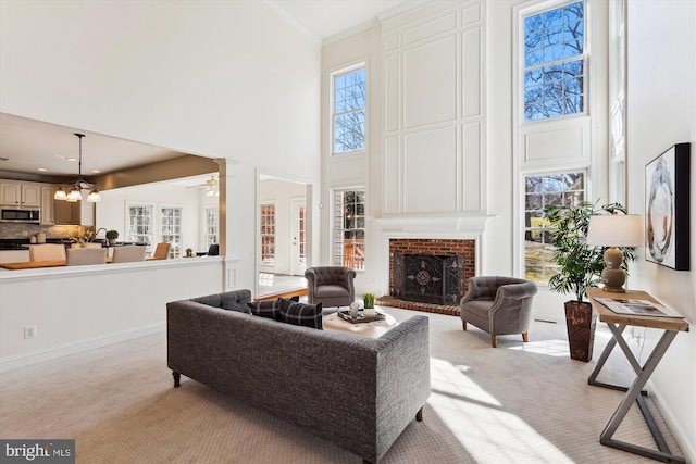 living area featuring baseboards, light colored carpet, ornamental molding, a fireplace, and a high ceiling