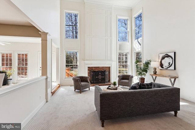 living area with a brick fireplace, baseboards, carpet flooring, a high ceiling, and ornate columns