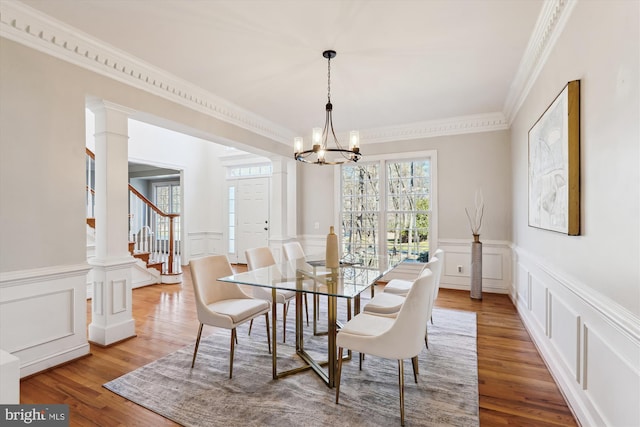 dining space featuring wood finished floors, decorative columns, ornamental molding, a decorative wall, and a notable chandelier