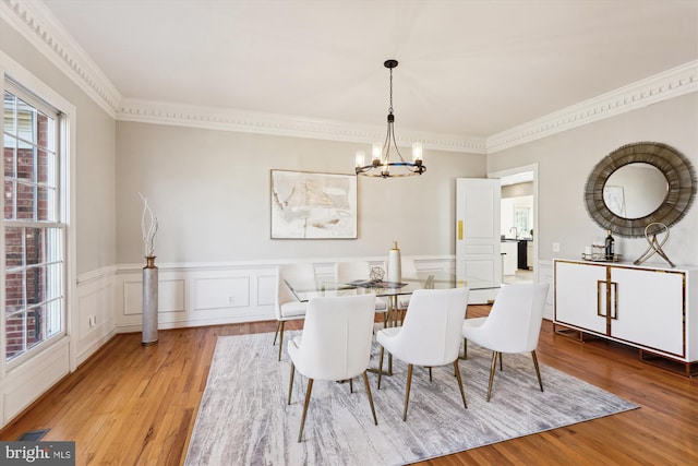 dining room featuring a chandelier, a wainscoted wall, wood finished floors, and crown molding