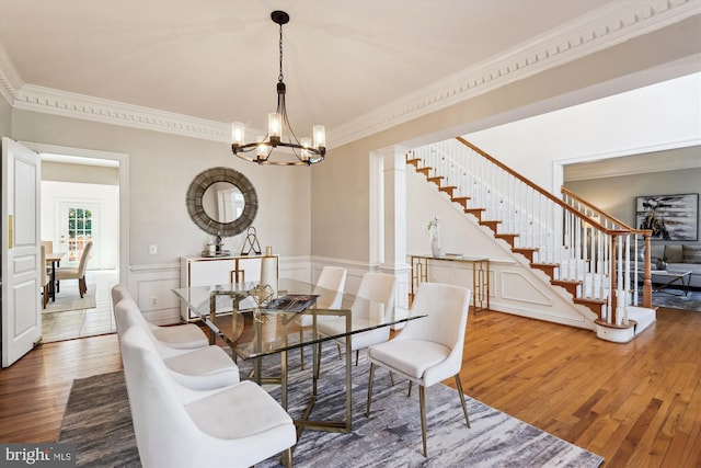 dining space with a notable chandelier, wood finished floors, wainscoting, crown molding, and stairs