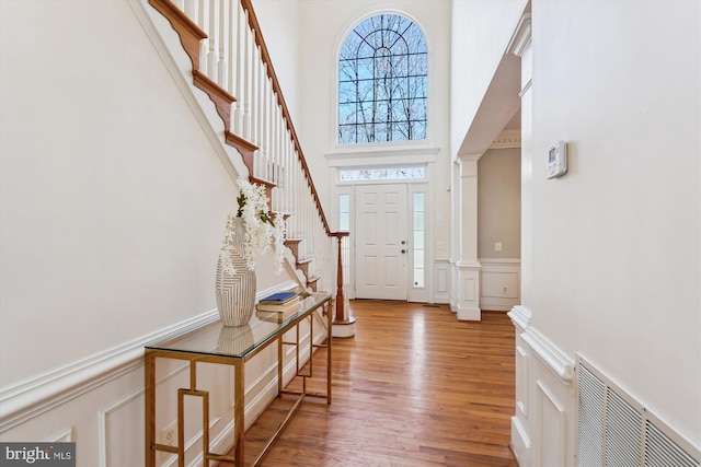 entrance foyer with wood finished floors, visible vents, a high ceiling, decorative columns, and a decorative wall